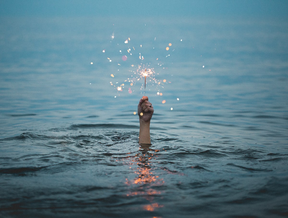 A hand, holding a sparking firecracker rising out of the water