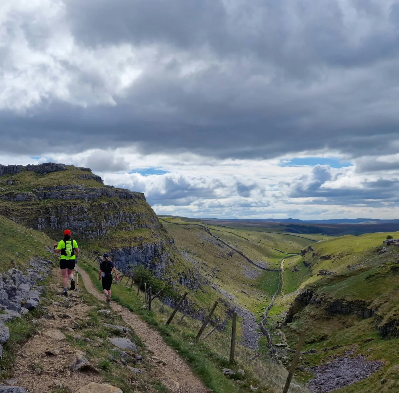 Two runners on a trail above a limestone valley