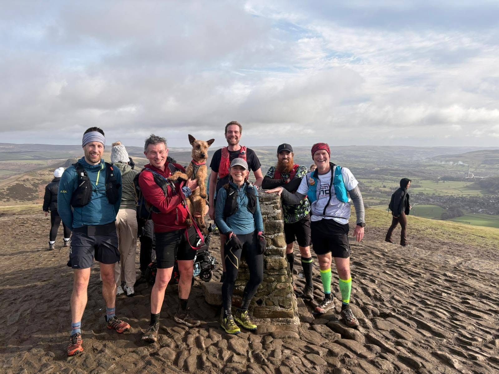 A group of runners and a dog smiling together at a summit