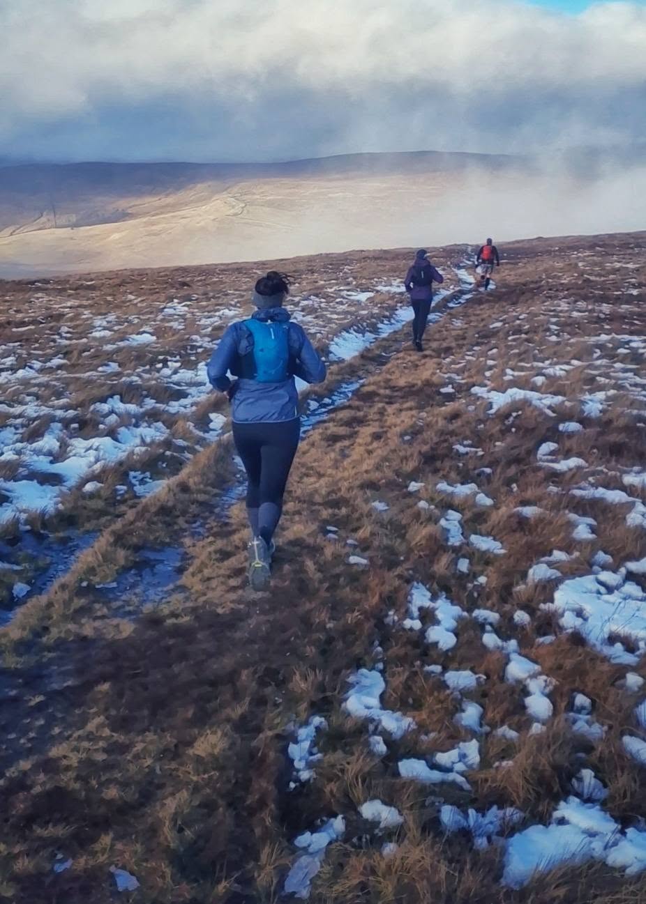 Runners following a snowy trail into the hills