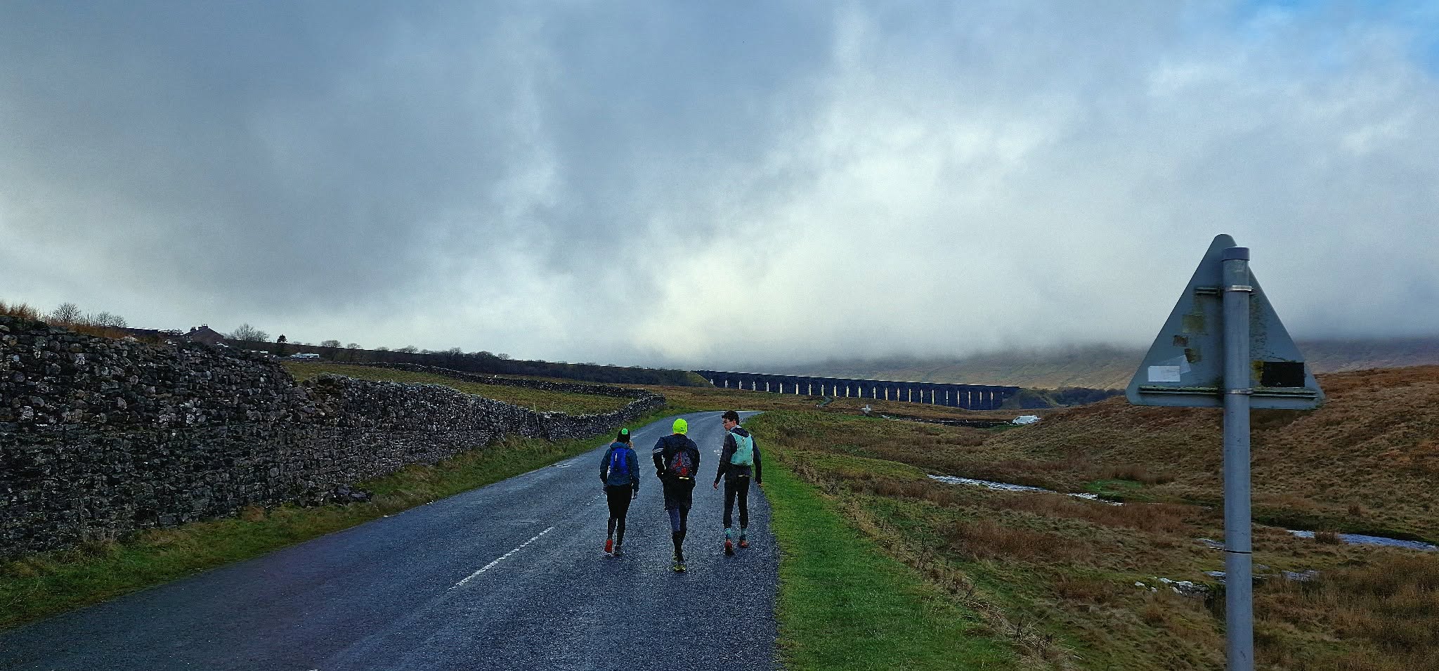 Three runners heading towards a distant viaduct beneath low cloud
