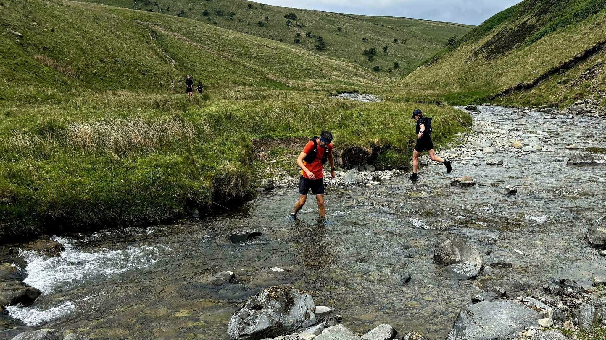 Runners crossing a stream together on a green valley trail