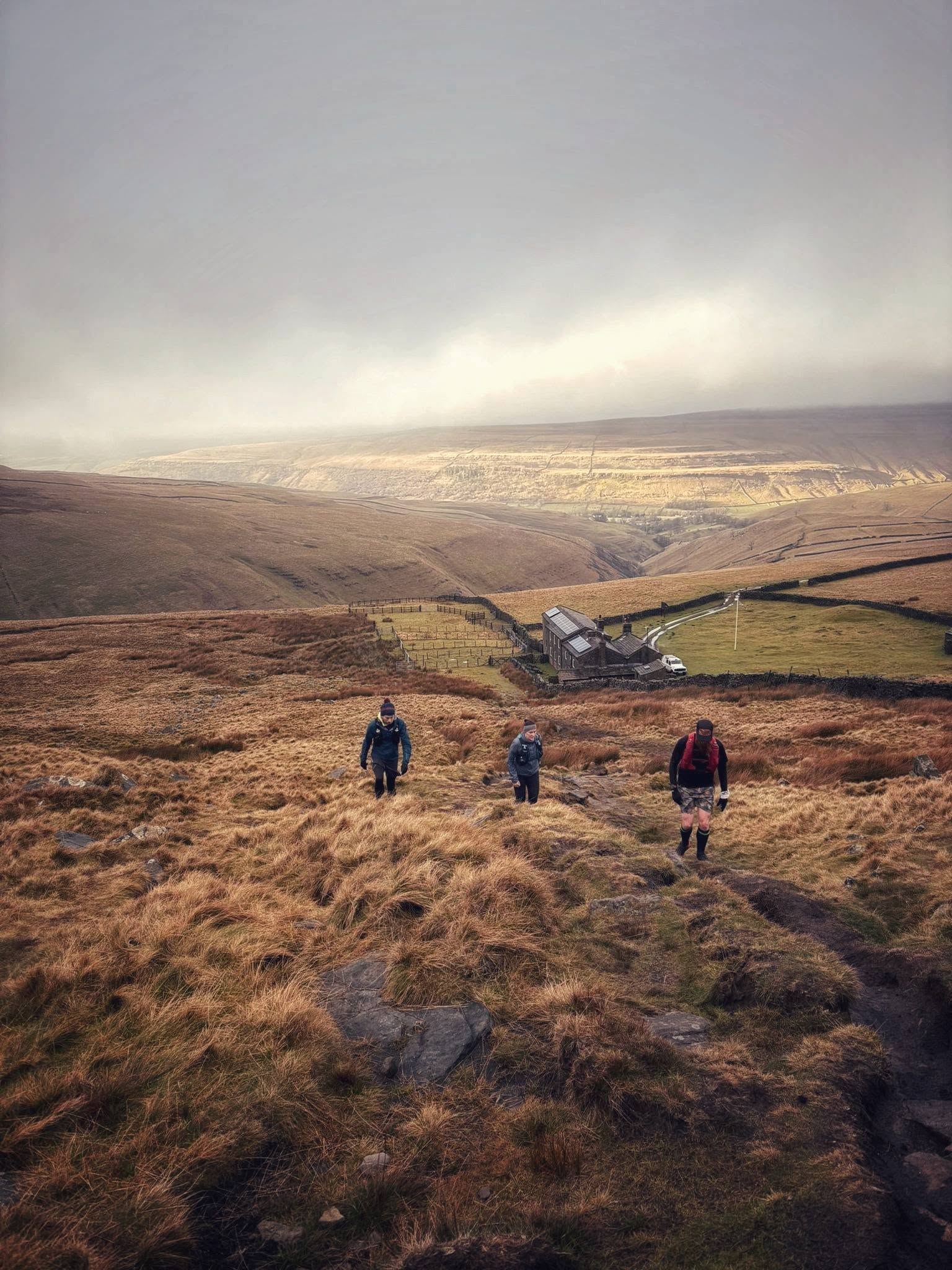 Runners climbing a moorland slope beneath a bright break in the cloud