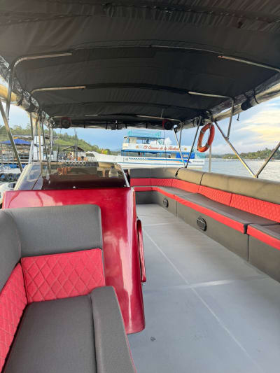 El planchón rojo por dentro en el muelle, con parlantes en las bancas