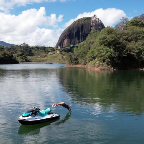 Rider diving off a jet ski into Guatapé Lake with El Peñol rock in the background