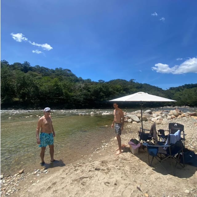 Amigos en la playa del río con el picnic montado bajo un parasol