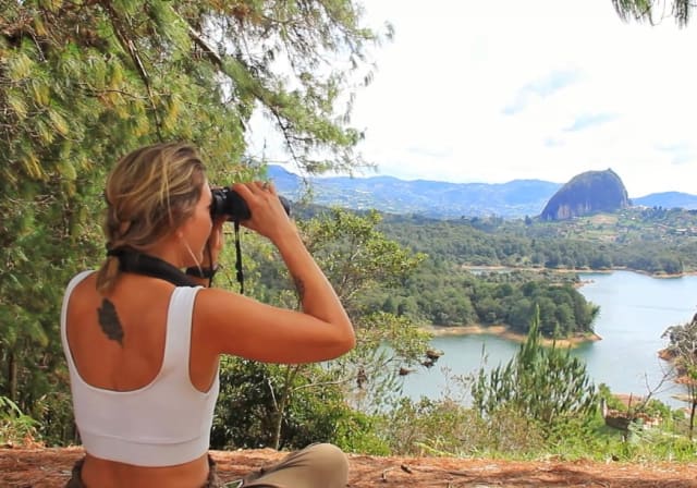 Observadora de aves con binoculares en un mirador sobre el embalse de Guatapé y la Piedra del Peñol
