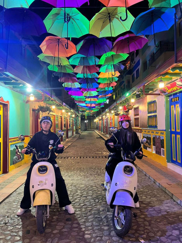 Riders on electric scooters under the umbrella street at night in Guatapé