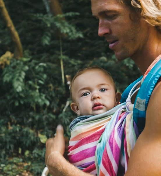 A man wearing baby in rainbow sling