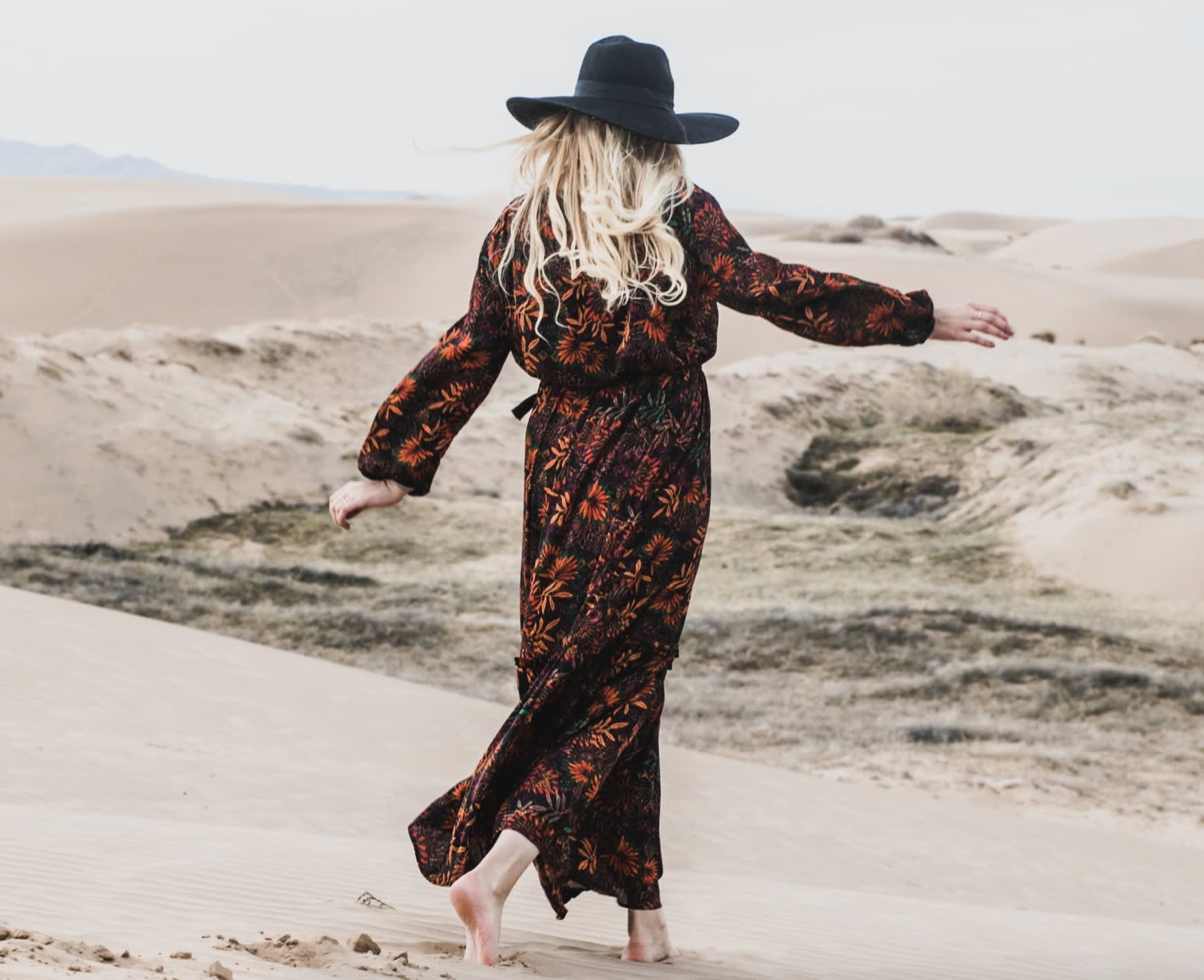 Woman wearing second-hand black floral maxi dress with a black fedora hat