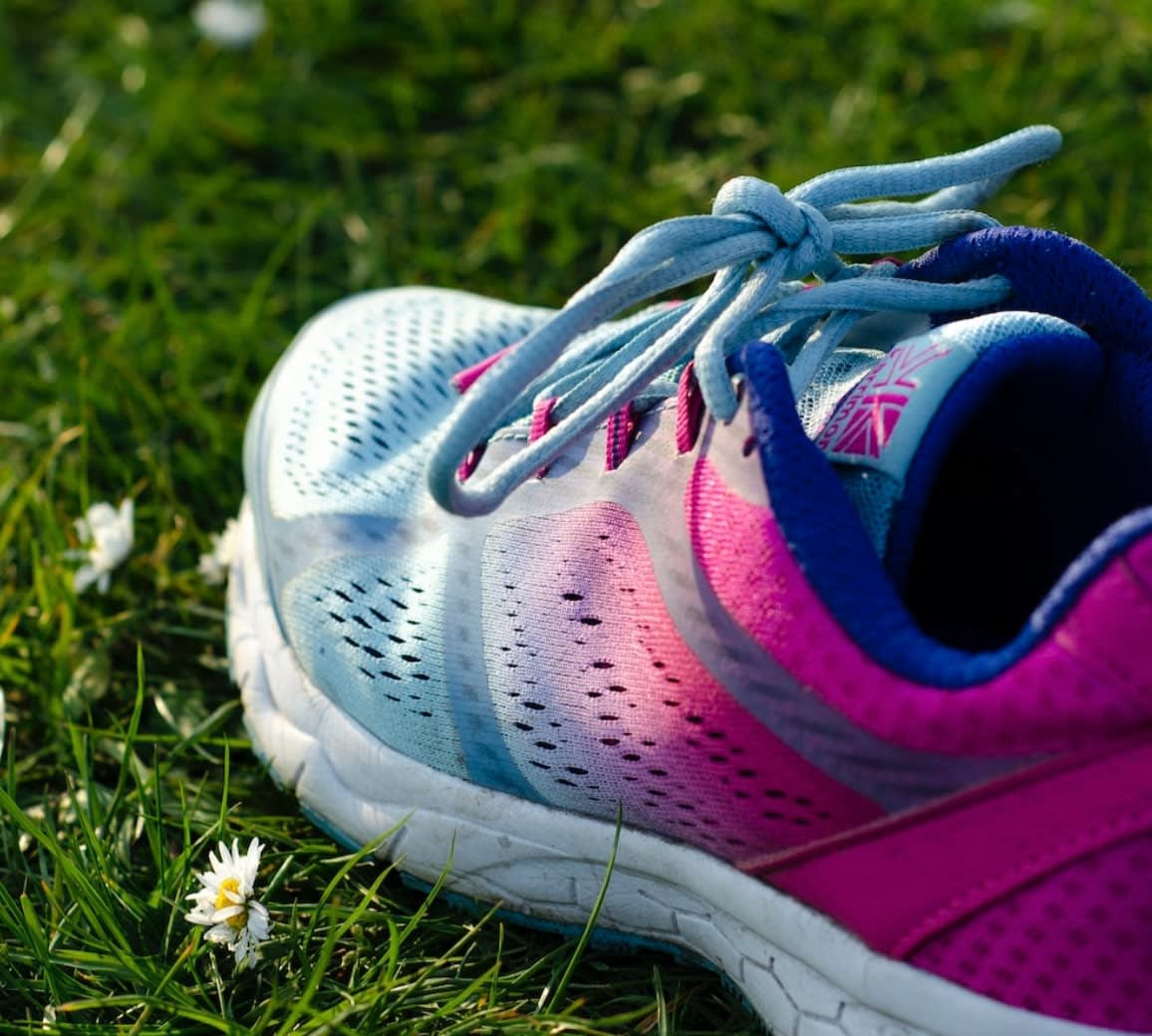 Pink and blue second-hand running trainers in a field of daisies