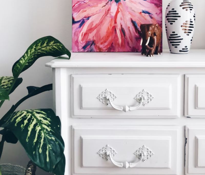 Wooden chest of drawers painted white in white room with pink painting