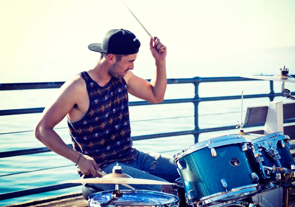 Man wearing retro tank top, playing the drums by the beach