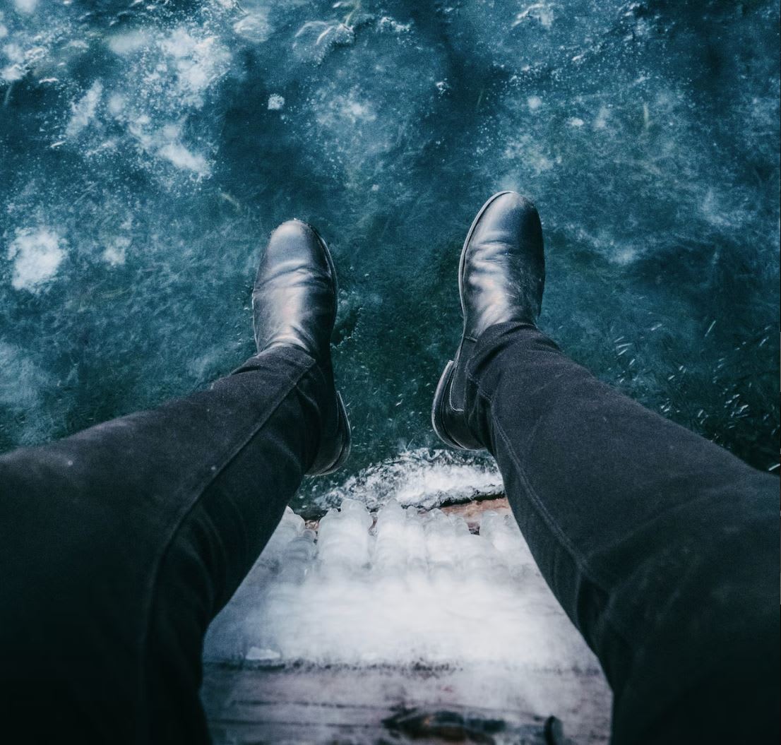 Man wearing black Chelsea boots overlooking some icy water