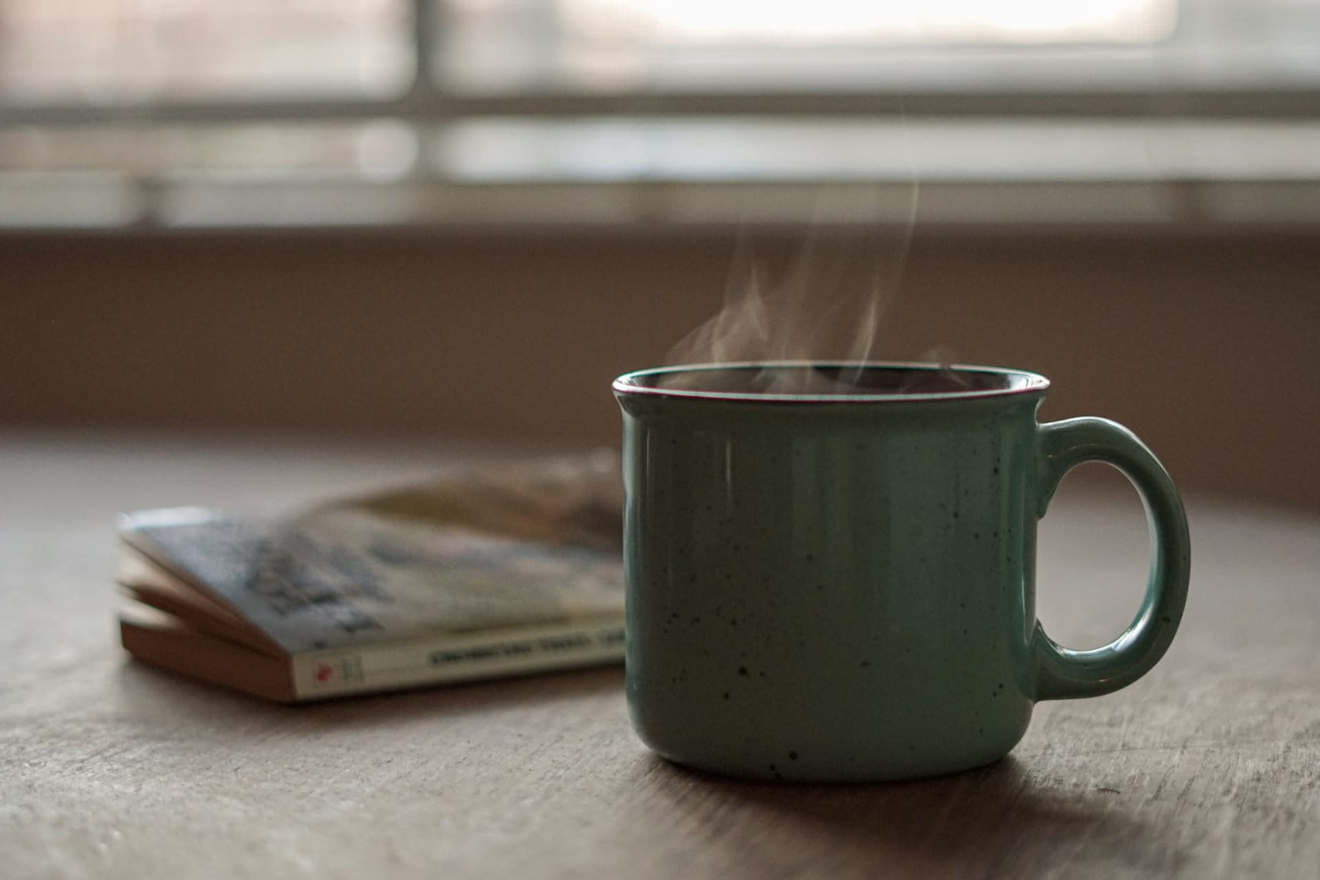 Coffe-filled mug and a book on coffee table