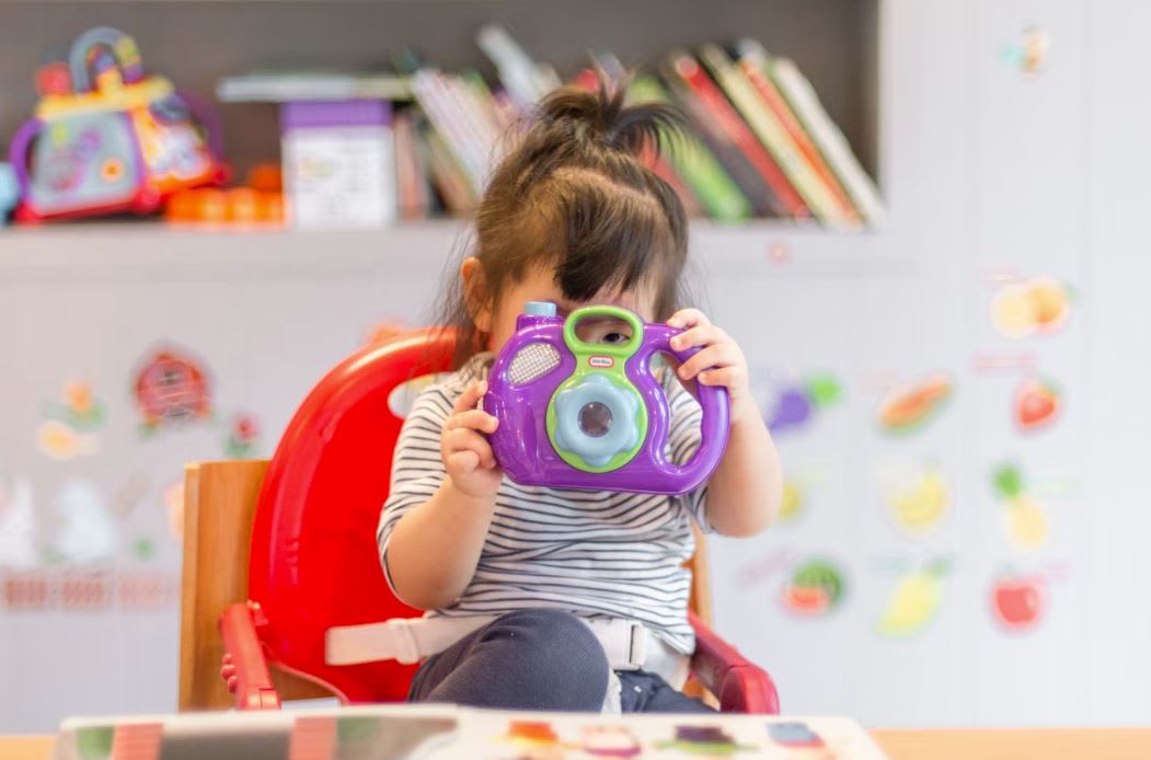 Little girl on high chair taking a picture on a purple camera