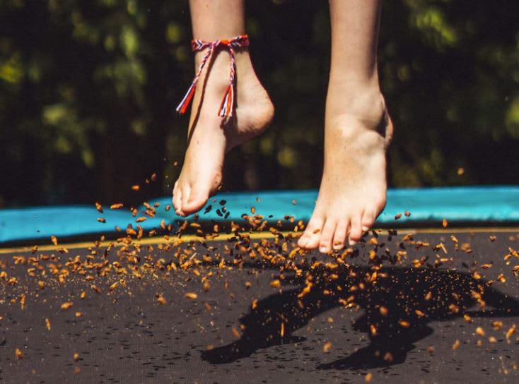 Kid's feet mid jump on a trampoline with leaves bouncing