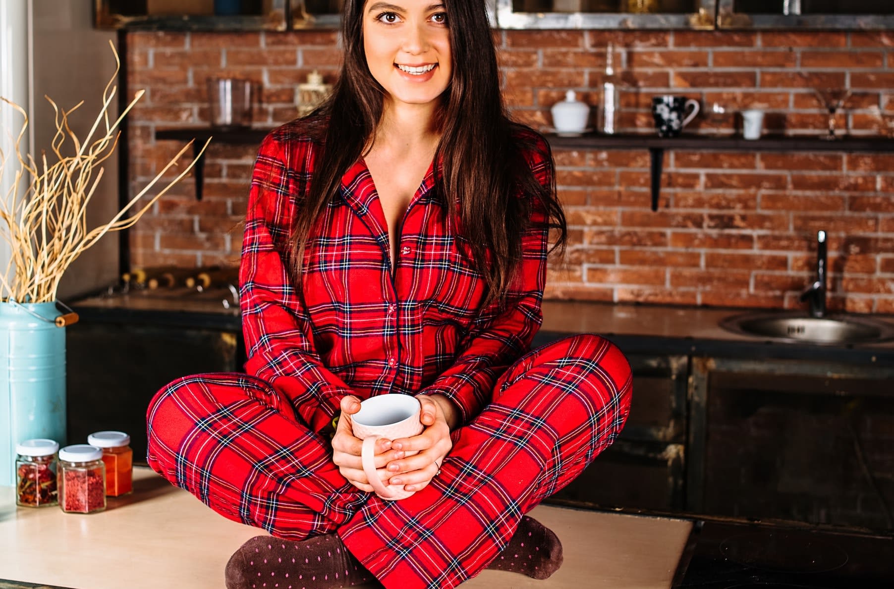 Woman sitting on kitchen table wearing red tartan pajama set