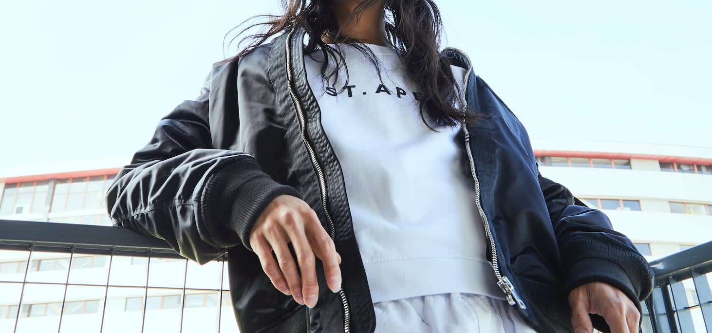 Woman leaning on fence whilst posing with her bomber jacket