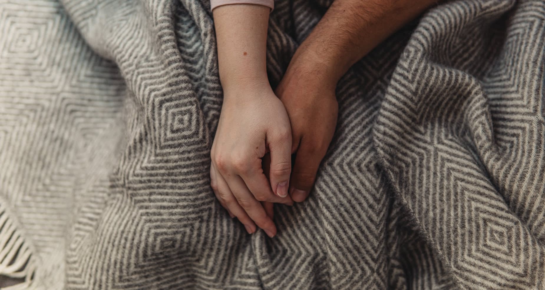 Two people comforting themselves with a cosy striped blanket