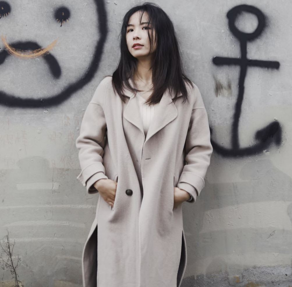 Women standing against spray painted wall in beige cashmere coat