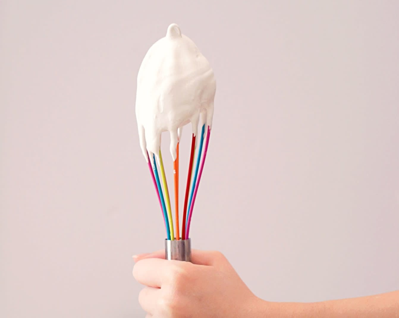 Kid holding up a multi coloured whisk with icing on it