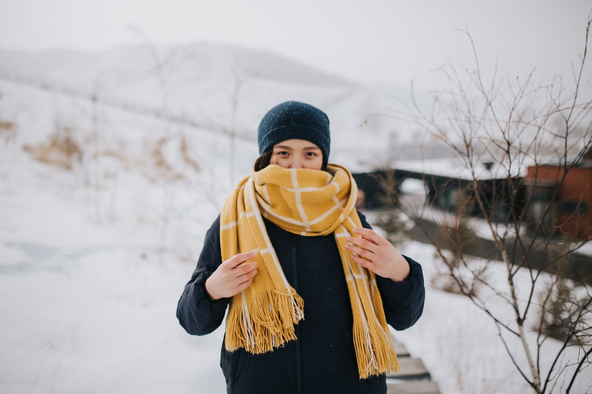 Woman wearing second-hand mustard scarf covering most of her face, with snowy background