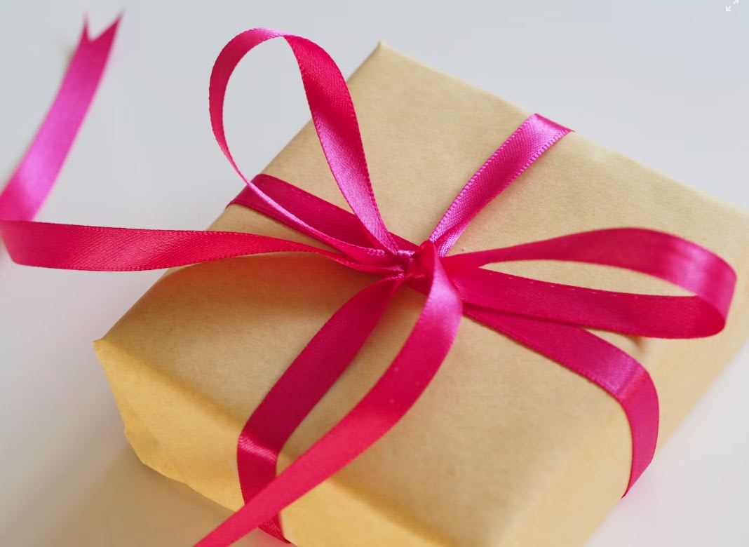 Small Christmas gift wrapped in brown paper and pink or red ribbon