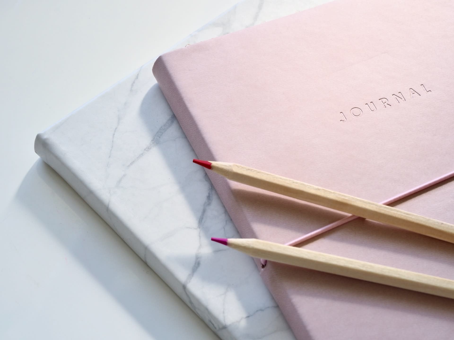 Pale pink and white jounals on white table with two pencils