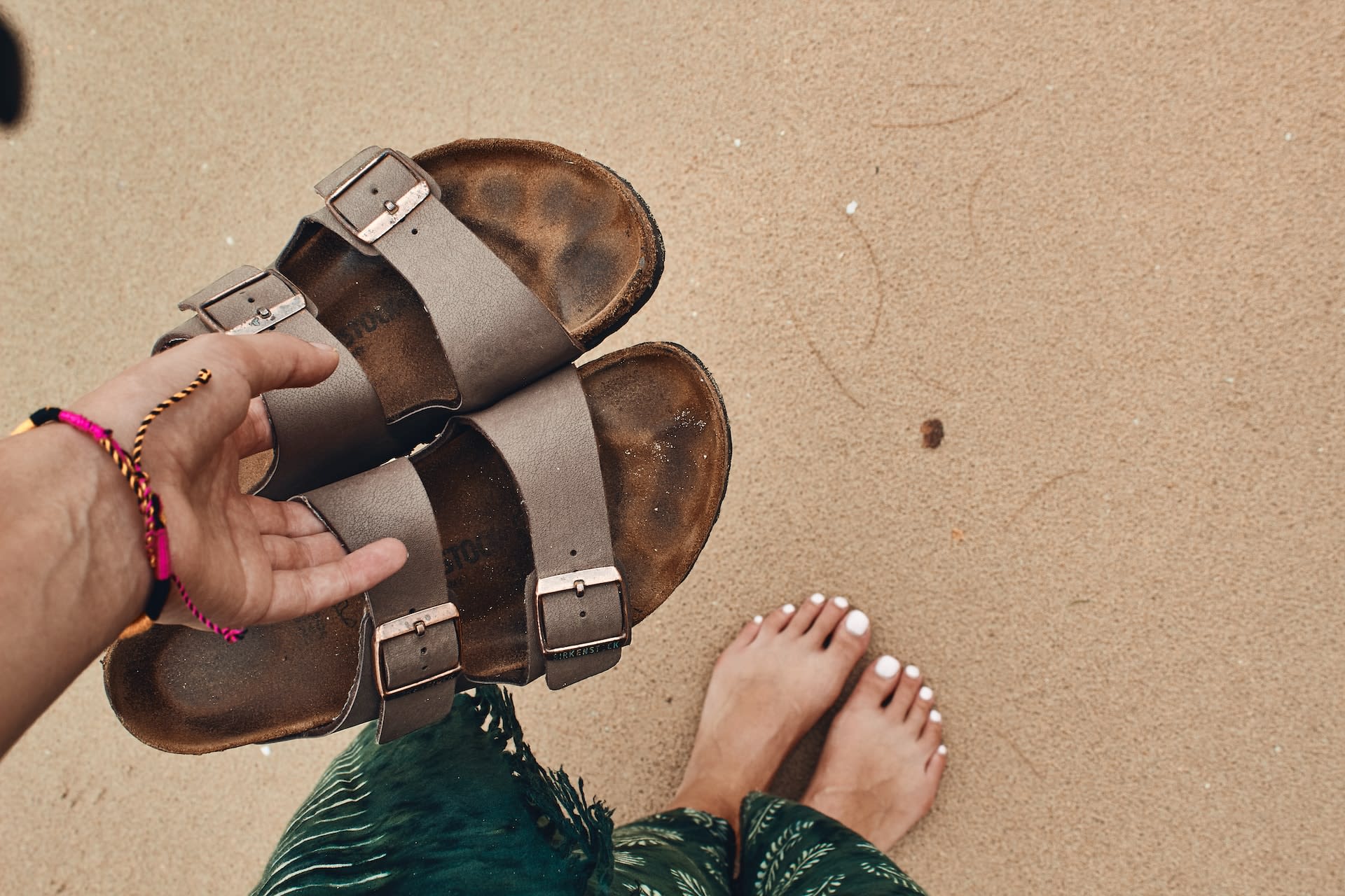 Woman carrying pre-loved brown leather sandals on the beach