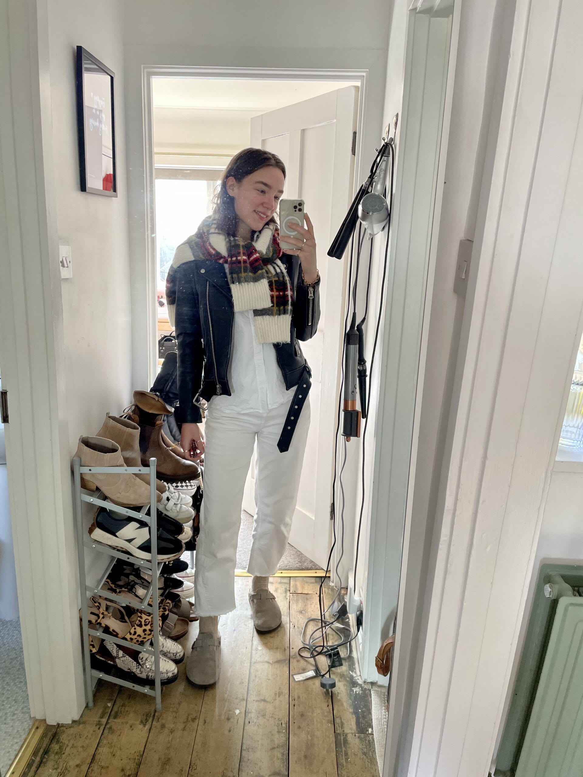 Iso Neville - casually put together - wearing checked jumper, black leather jacket, white shirt, wide leg trousers and taupe clogs or mules