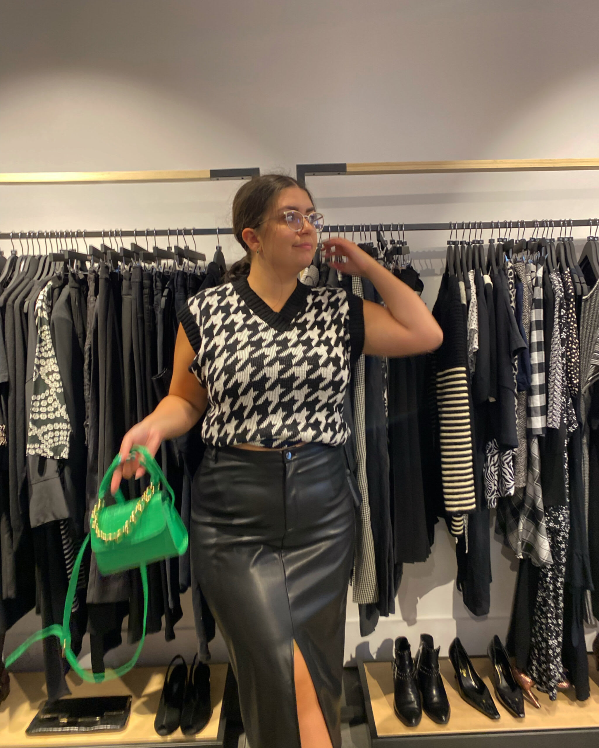 Amy Lorenz in preloved dogtooth sweater vest, black leather midi skirt with a green mini bag.