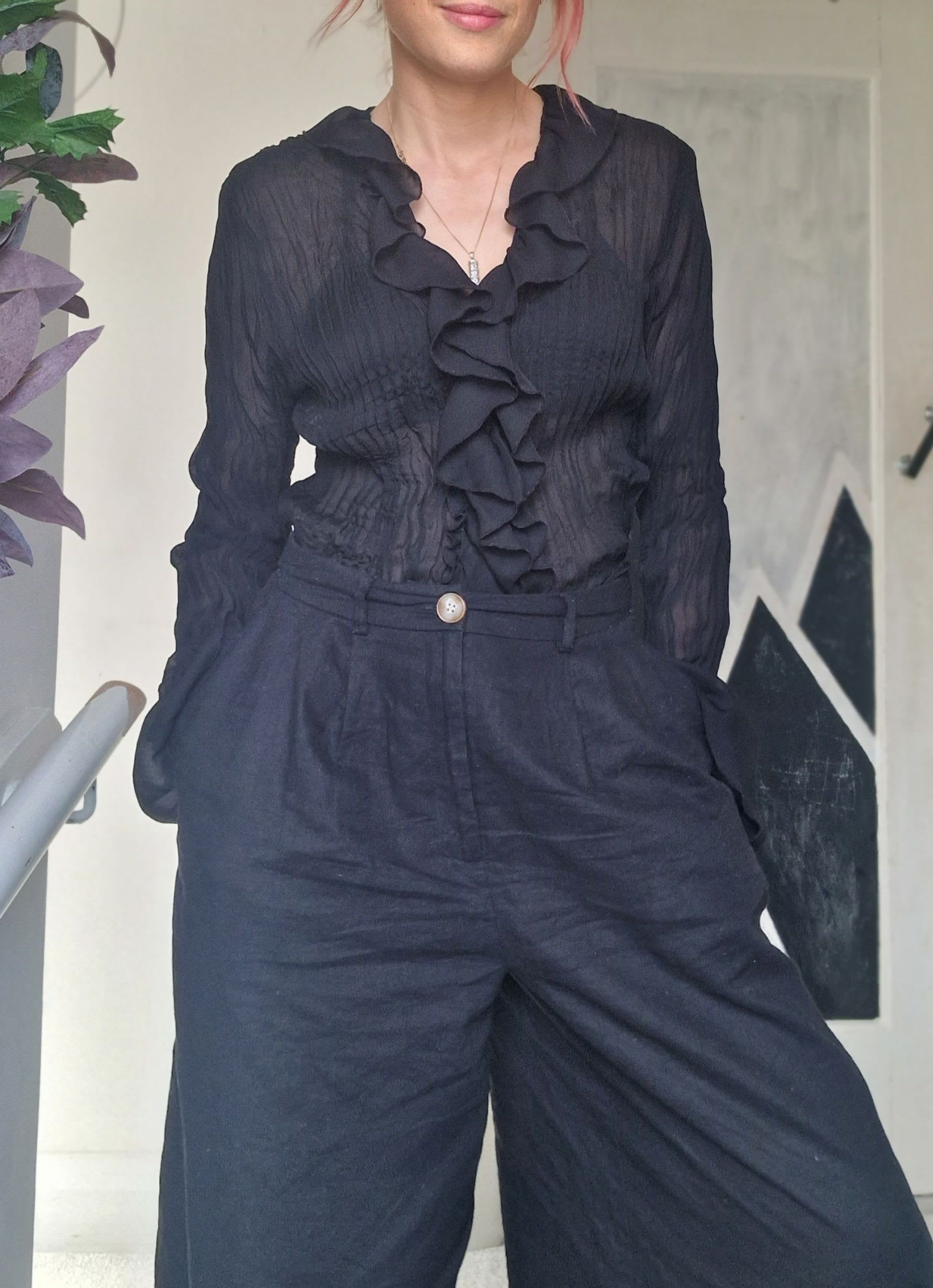 Pegz Preloved styling a sheer black ruffled shirt with black wide leg linen trousers.