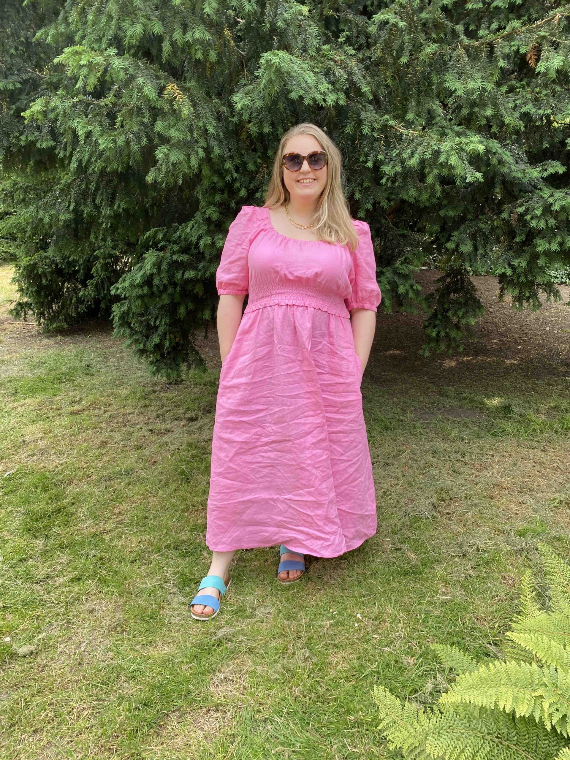 The thrifty edit wearing a pink dress and sunglasses standing in a park