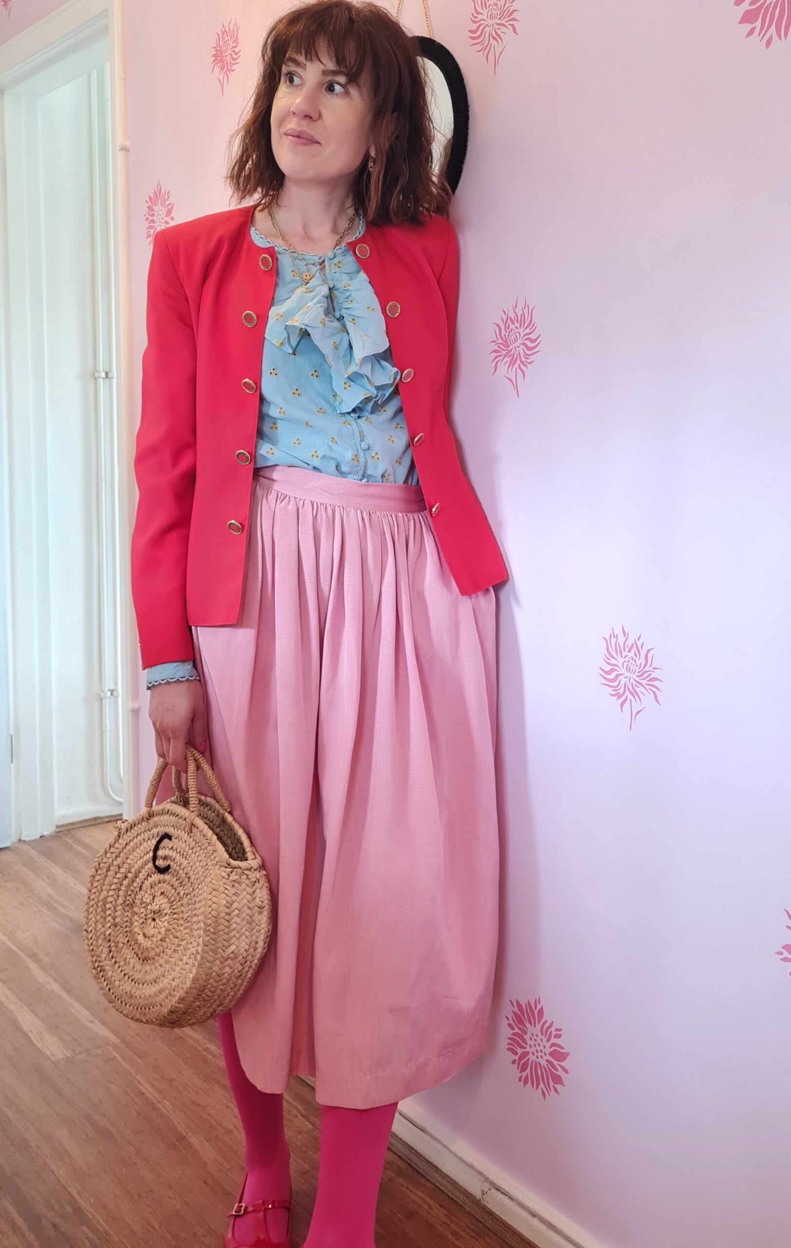 Carola stands before a pink wall in a mix and match pink outfit