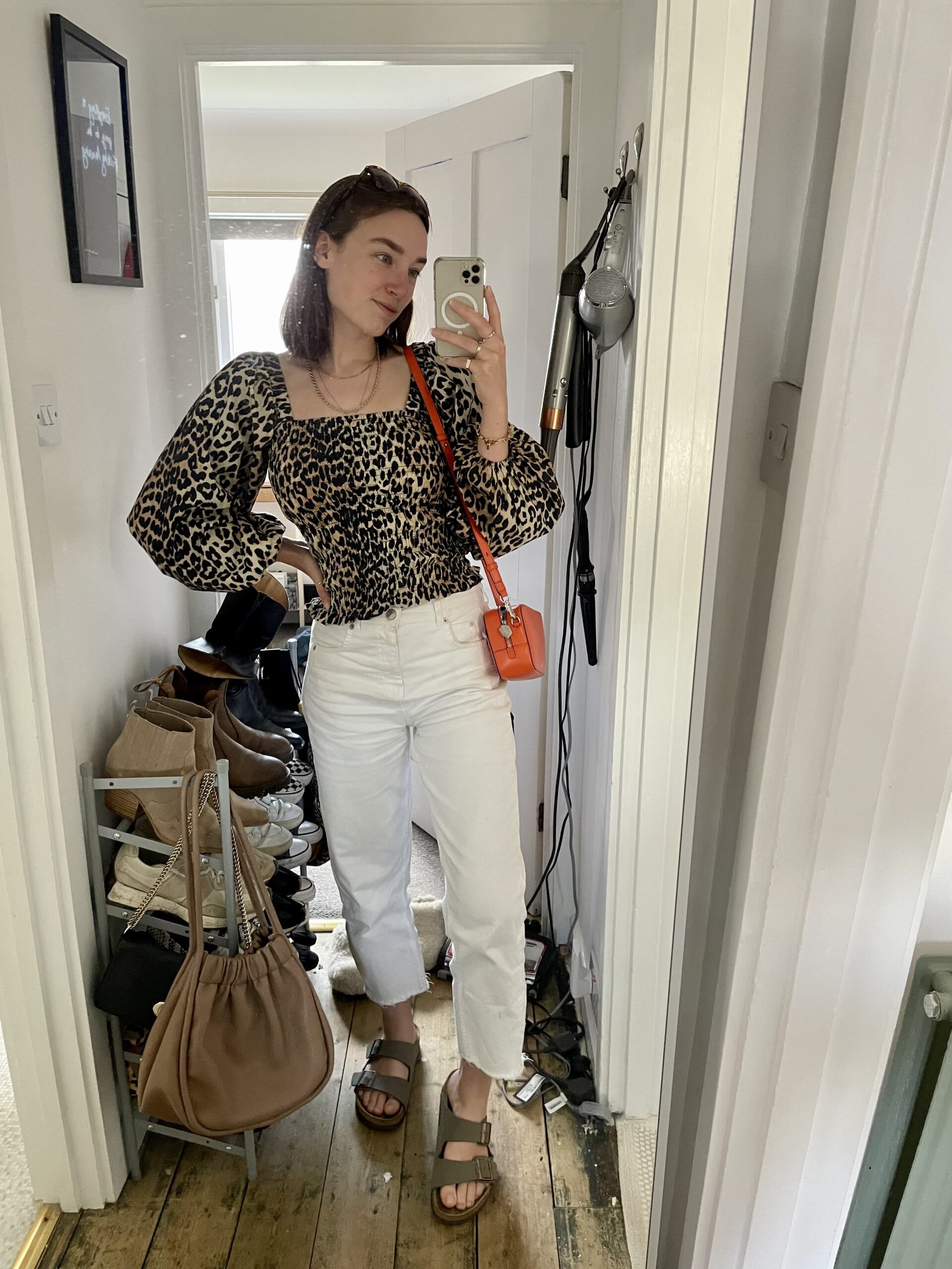 Iso wearing a balloon sleeved leopard print top with white mom jeans, Birkenstock sandals and an orange handbag.