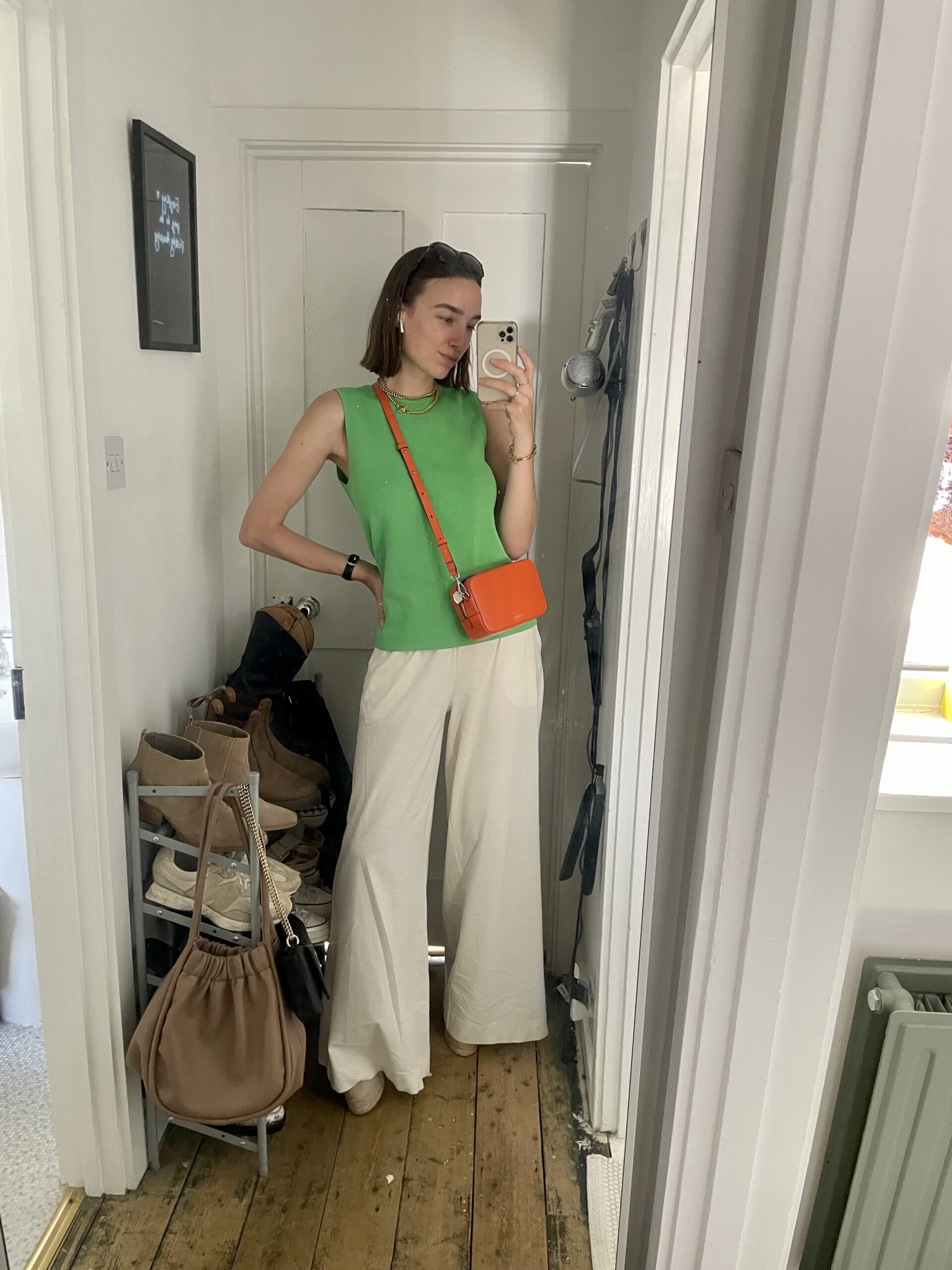 Iso wearing a green tank top with white trousers, espadrille wedges and an orange bag.