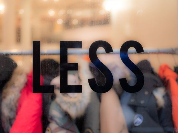 the word less on a window, with clothes blurred out behind it to depict say no to new