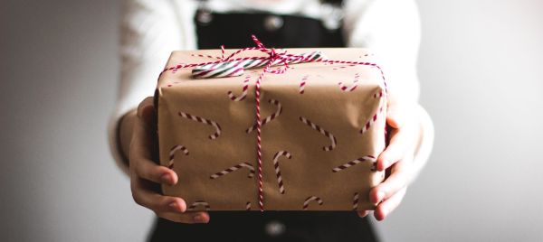 Girl holding out second-hand Christmas present in brown paper wrapping