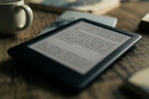 Second-hand kindle by mug on wooden desk