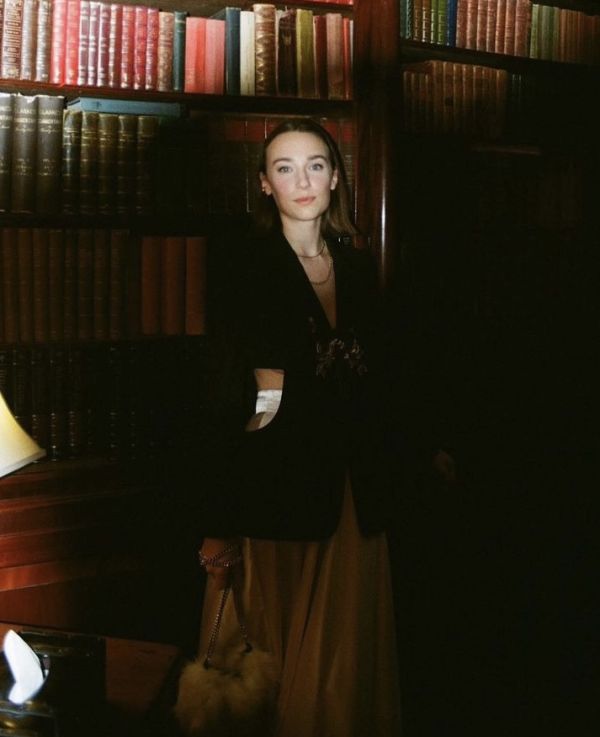 Iso Neville standing infront of a book case in black blazer and maxi skirt at fashion week