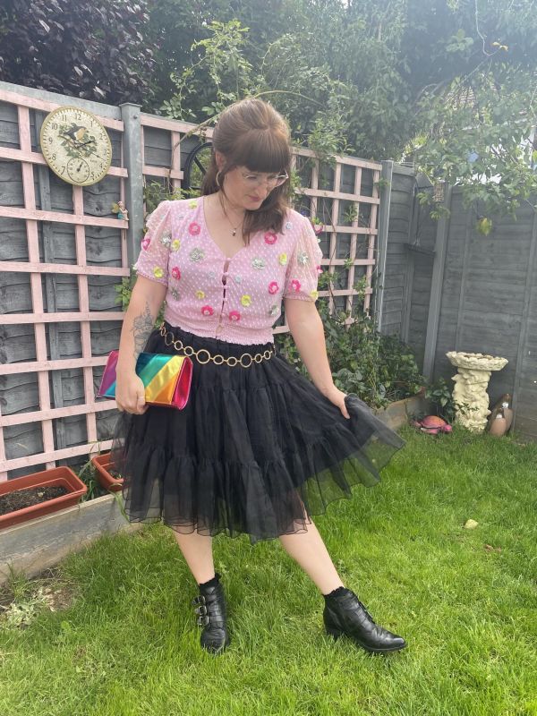 Little Splash styling a maximalist outfit with a tulle skirt, pink top, boots and a rainbow handbag.