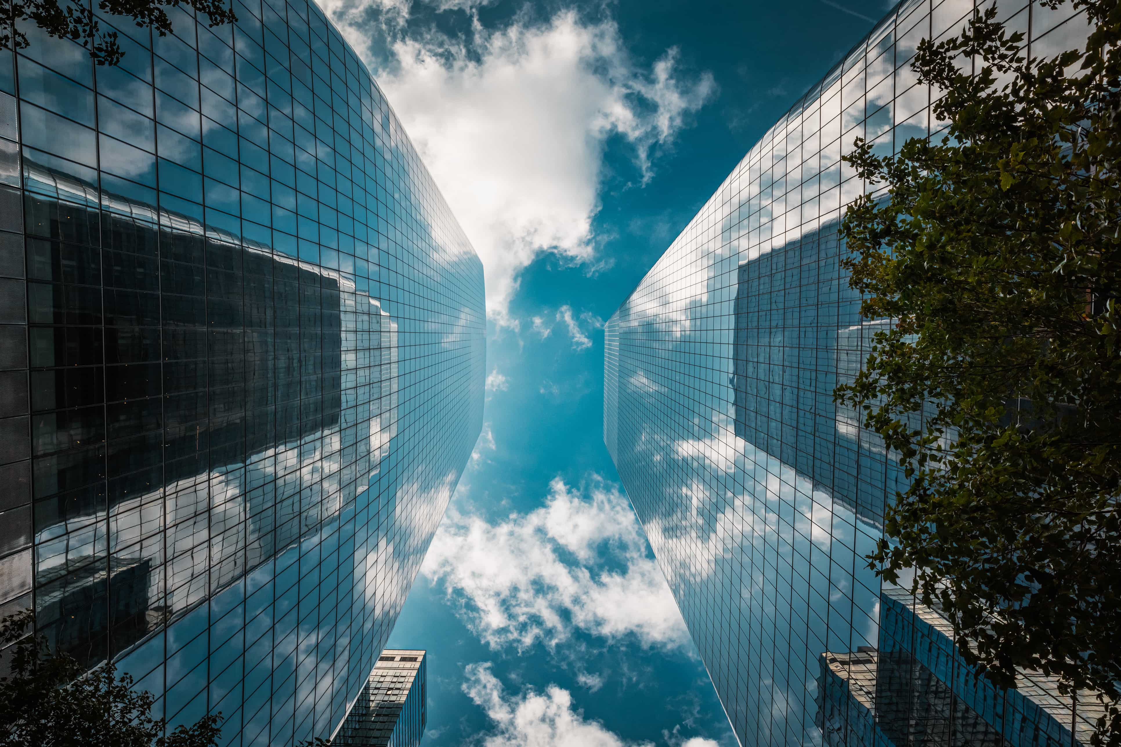 Looking up at tall glass buildings with a blue sky full of clouds