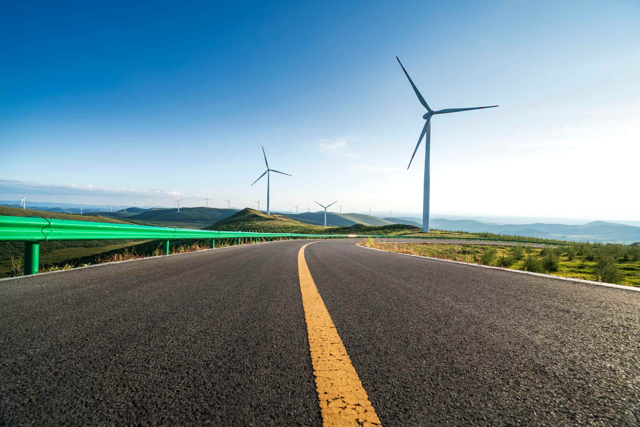 road with wind turbine in the background against blue sky