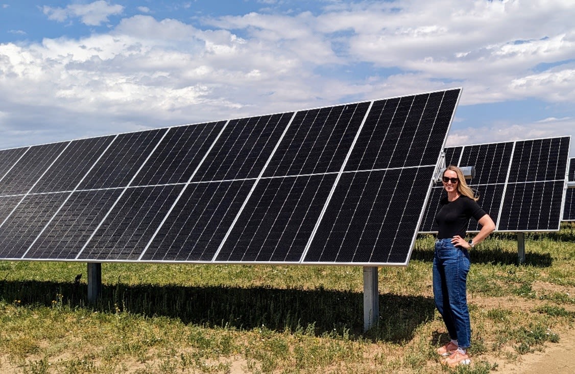 woman standing next to a solar panel in a field