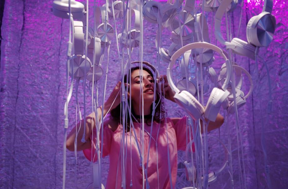 https://www.pexels.com/photo/photo-of-woman-wearing-pink-shirt-standing-near-white-headphones-against-purple-background-3812712/