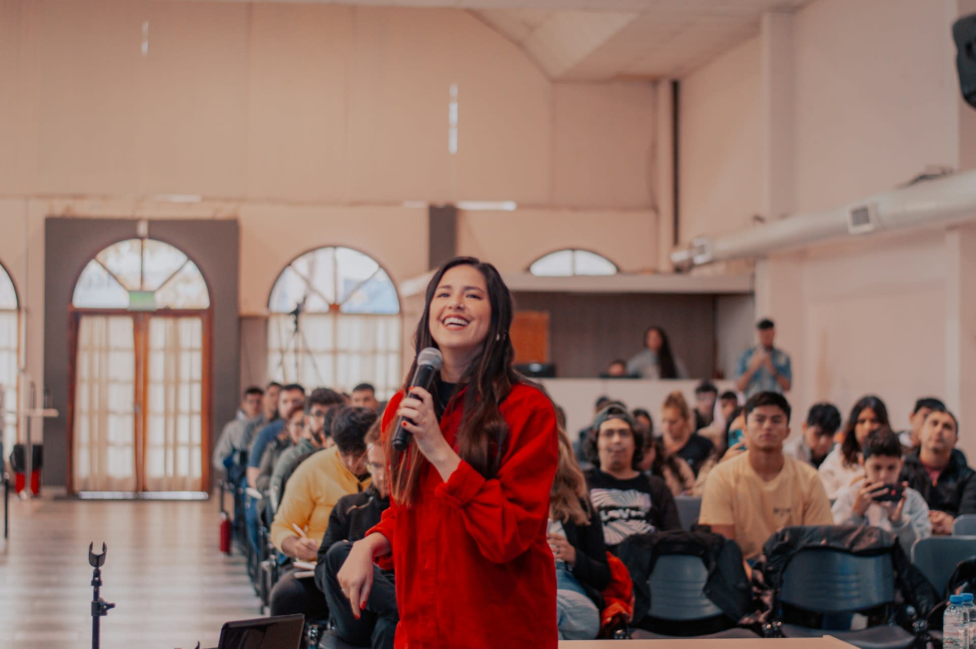 https://unsplash.com/photos/a-woman-standing-in-front-of-a-crowd-holding-a-microphone-NK02ShlfWDM