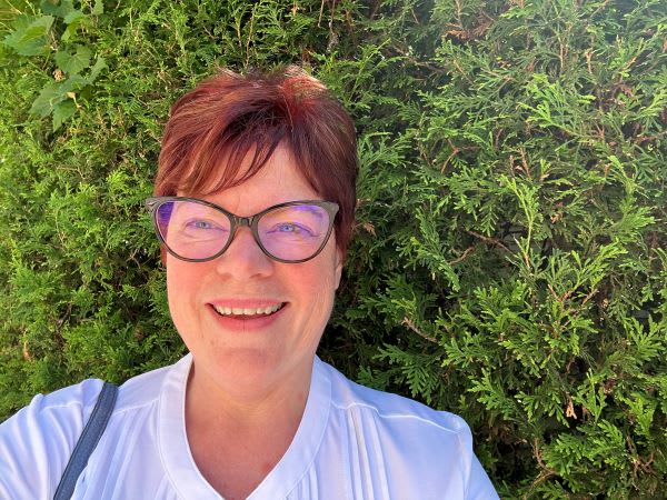 Image d’une femme souriante aux cheveux courts et roux et portant des lunettes.