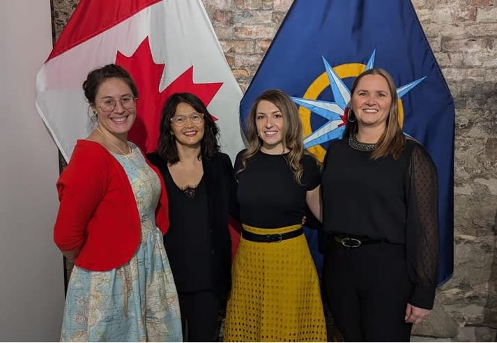 An image of 4 women smiling in front of two flags.