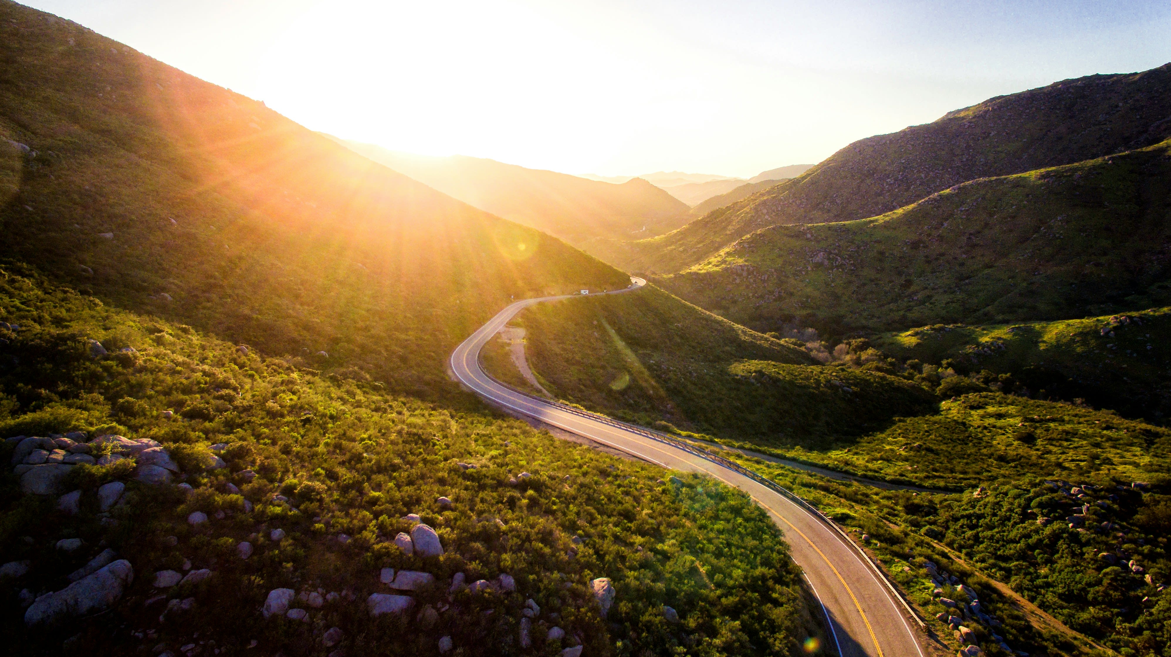 An image showing a winding road through the mountains at sunset.